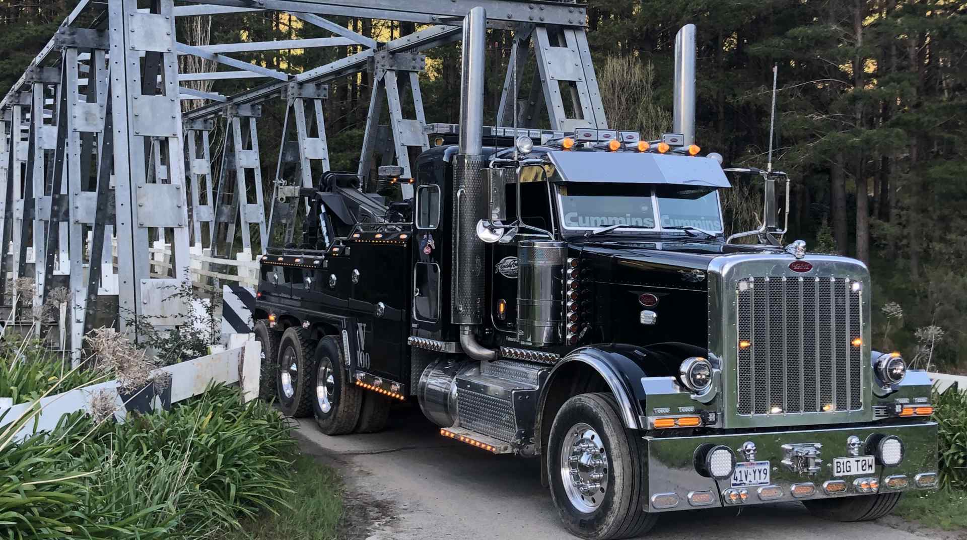 Truck Towing heavy recovery wrecker beside a steel truss bridge